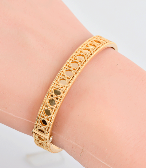 A gold-toned filigree bangle bracelet with openwork cutouts, shown worn on a wrist against a light background.